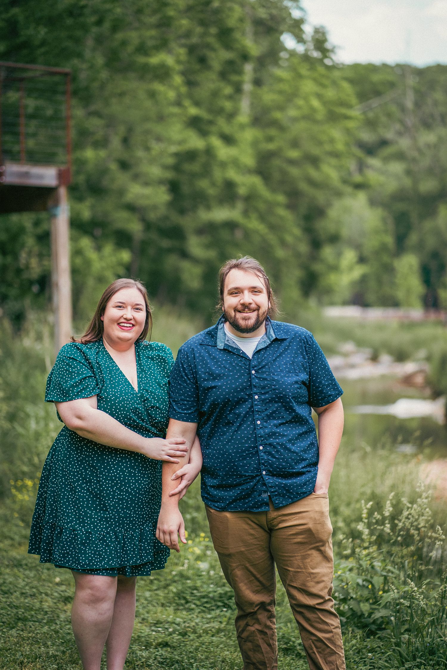 A couple in matching blue polka dot tops poses together in a lush green outdoor setting.