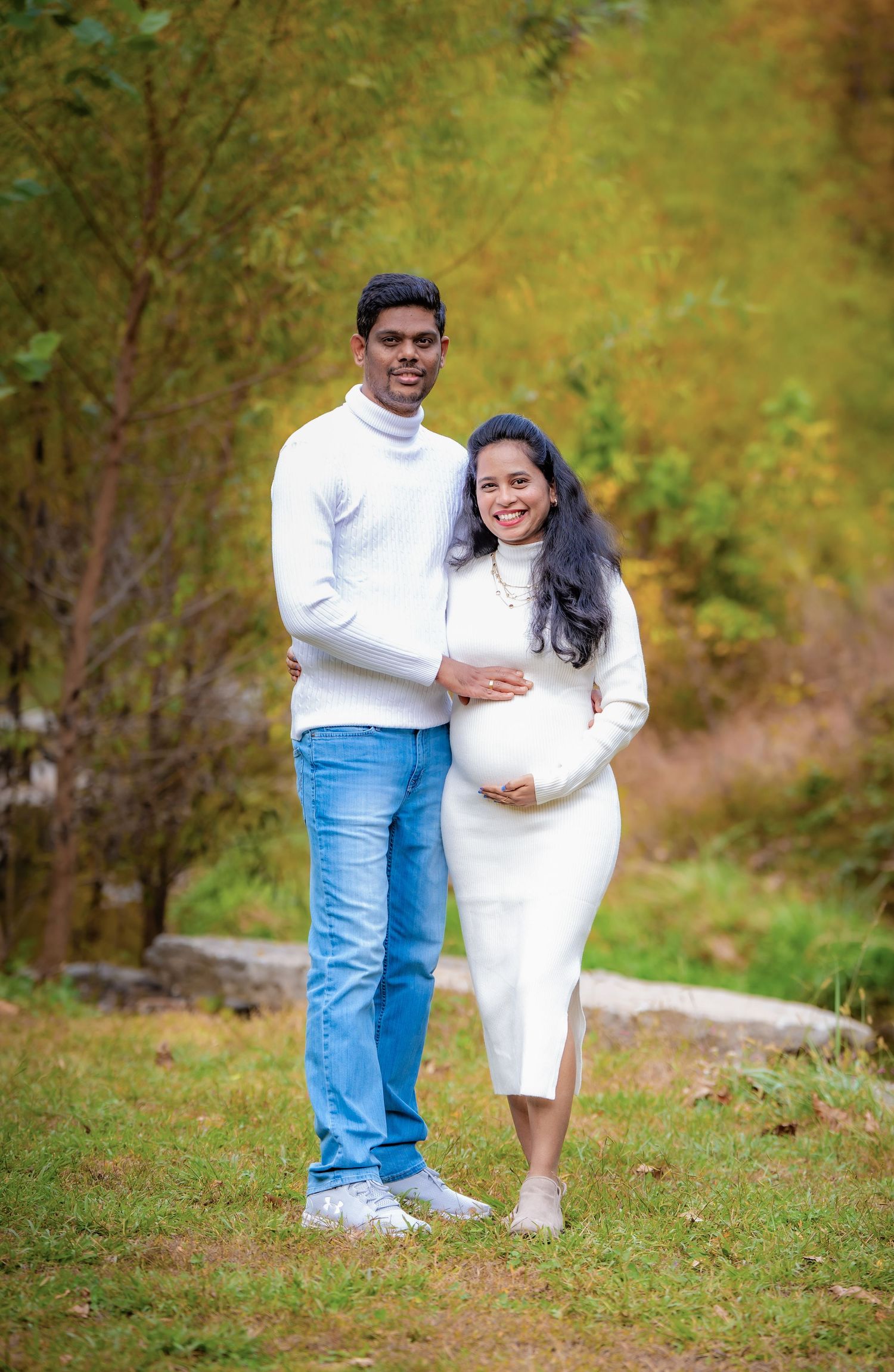 A couple poses together outdoors on a grassy hill during autumn with warm golden foliage in the background.