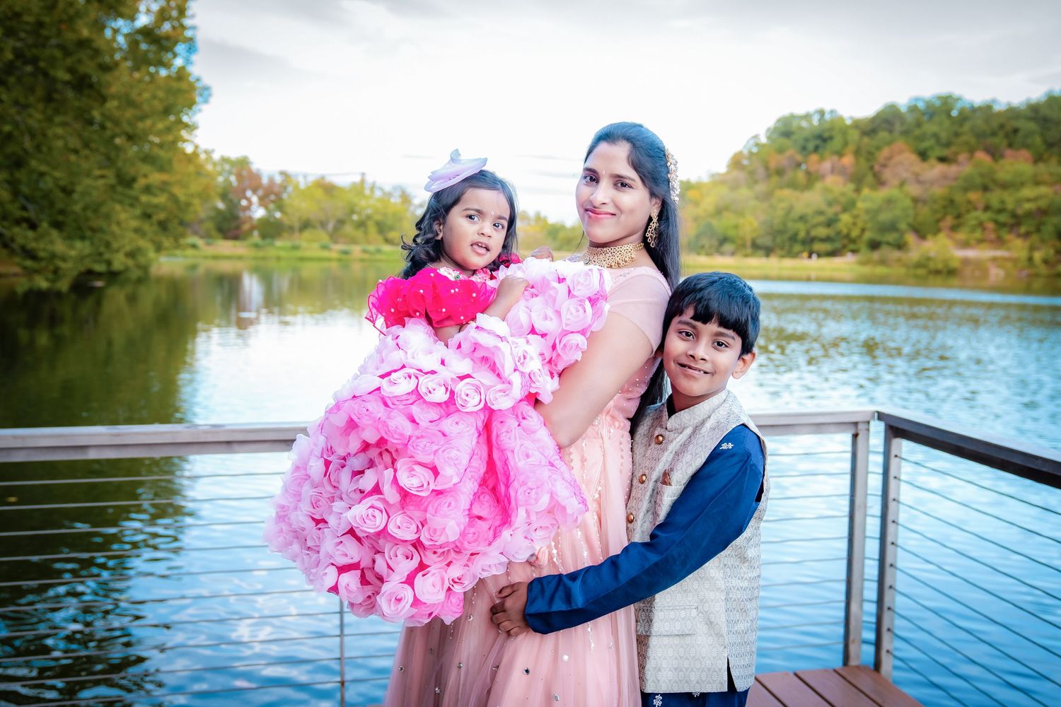 Family photoshoot by lake with pink dresses against water backdrop.