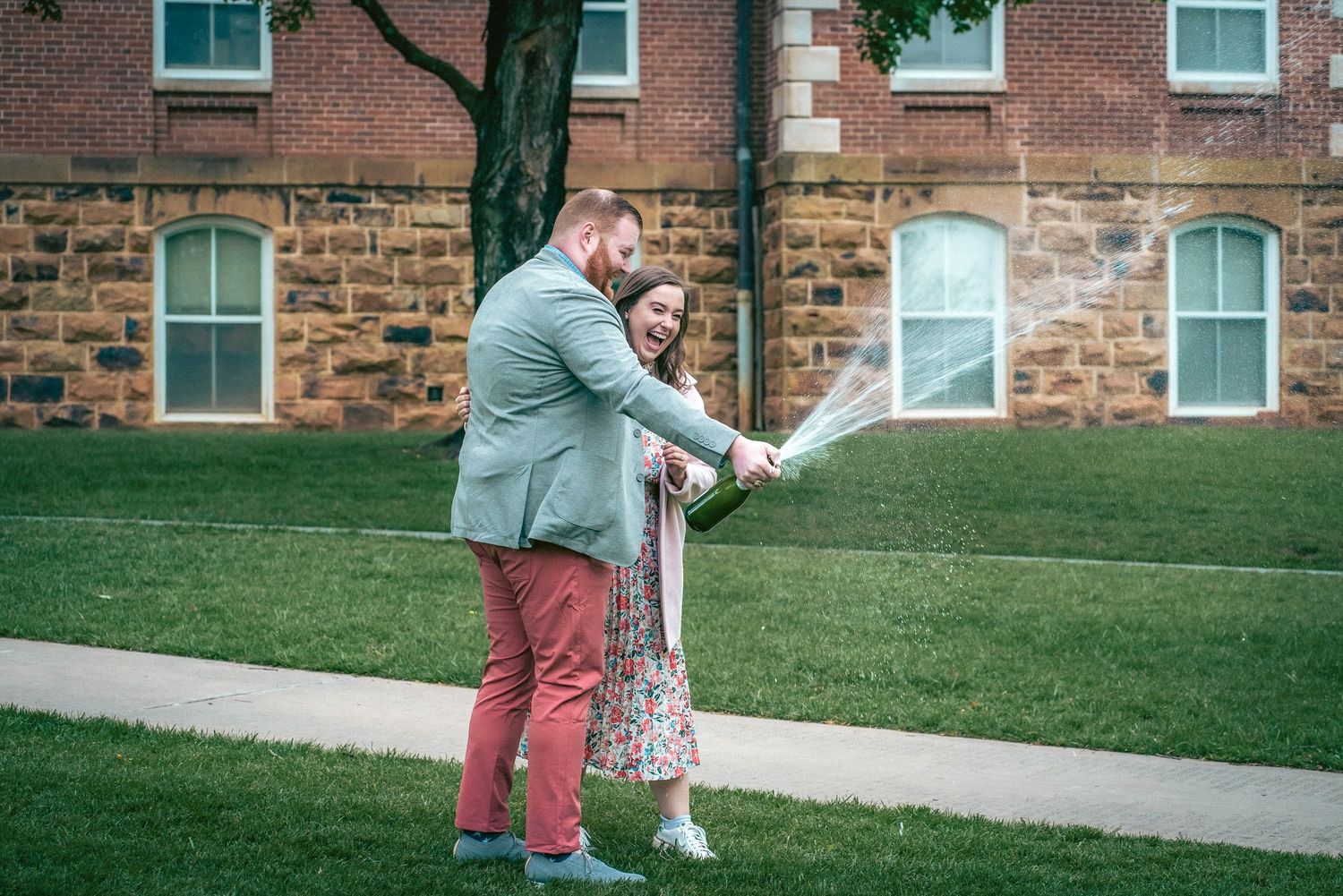 Couple walking and interacting on stone pathway near classic brick university building.