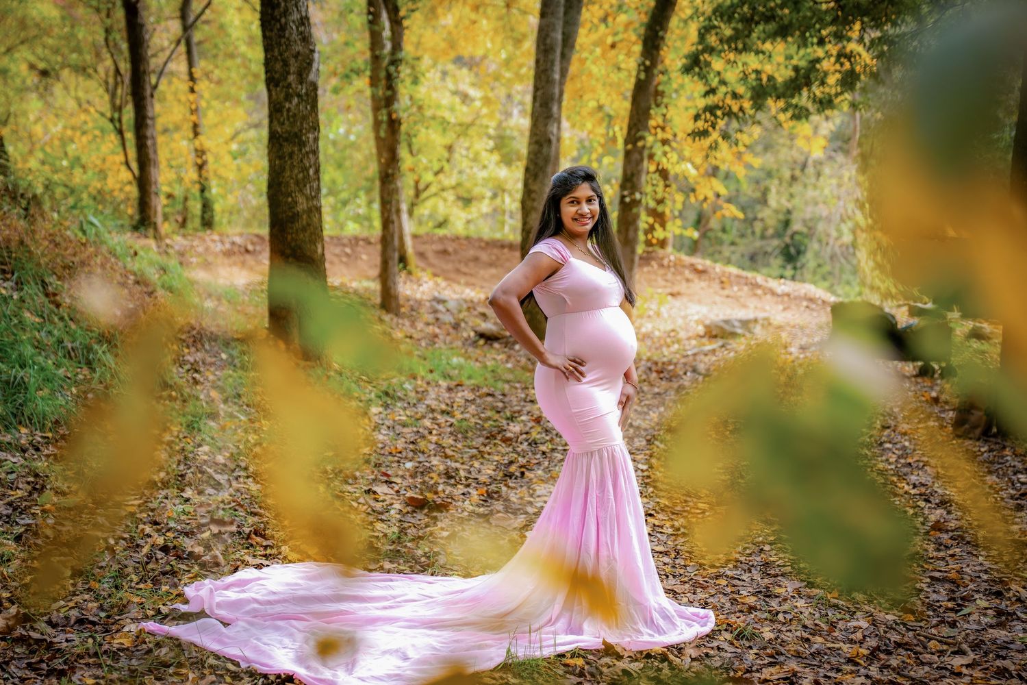 A flowing pink gown creates movement against autumn foliage in a forest setting.