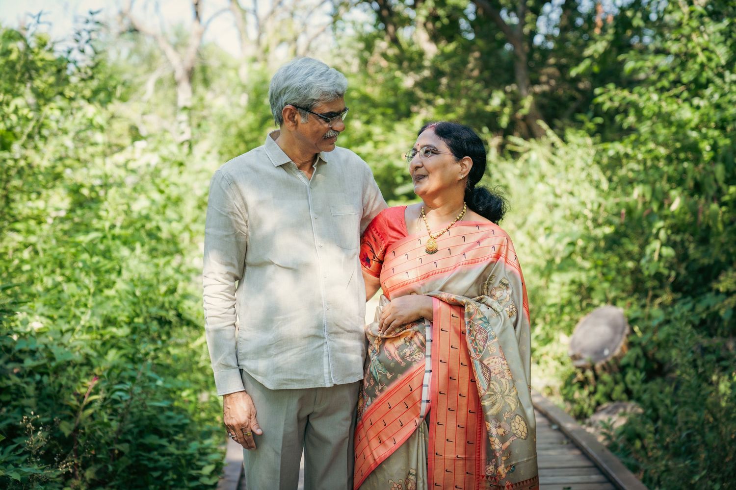 A couple in traditional Indian attire enjoys a tender moment outdoors among greenery.