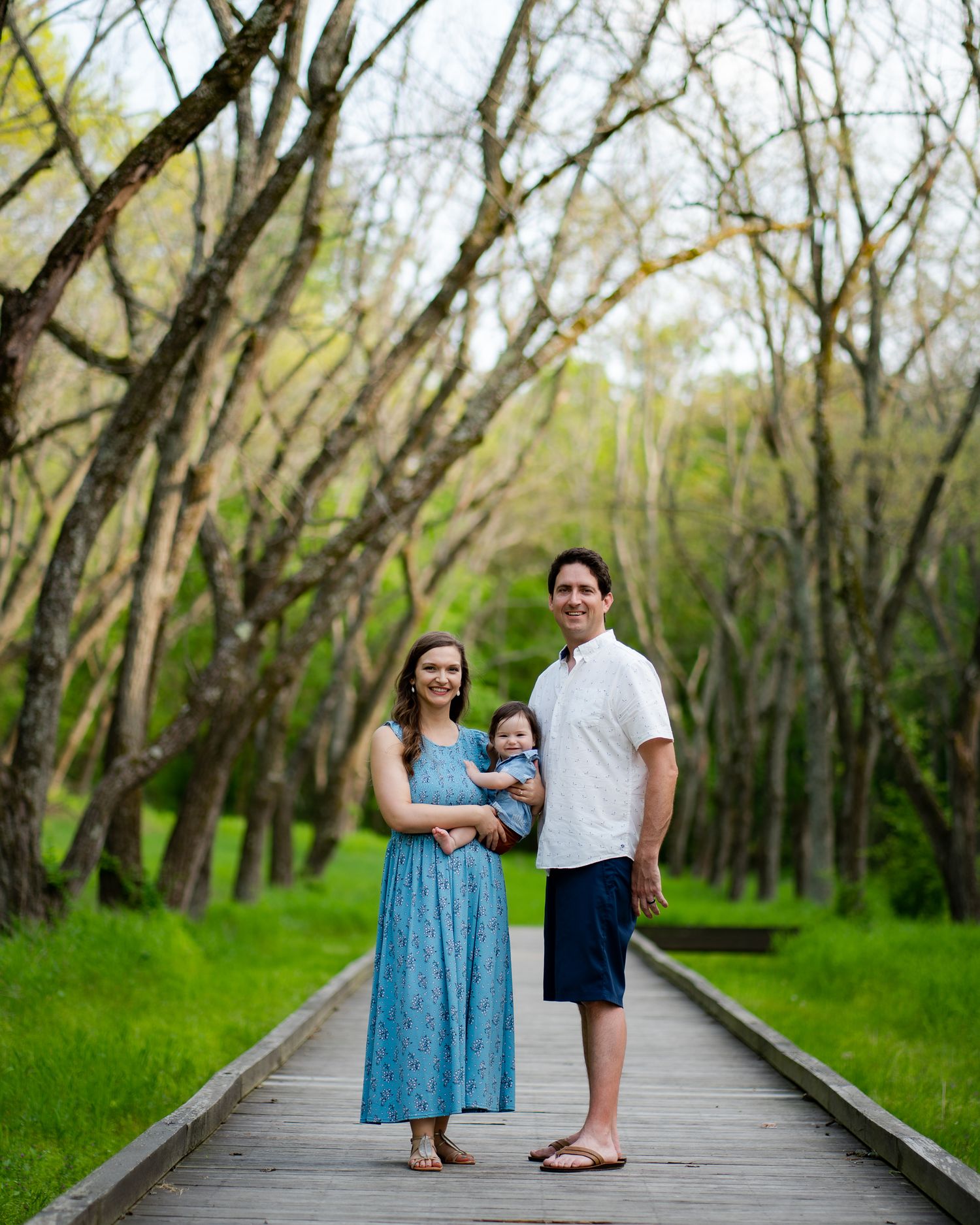 Couple walking along wooden boardwalk through wooded area in springtime.
