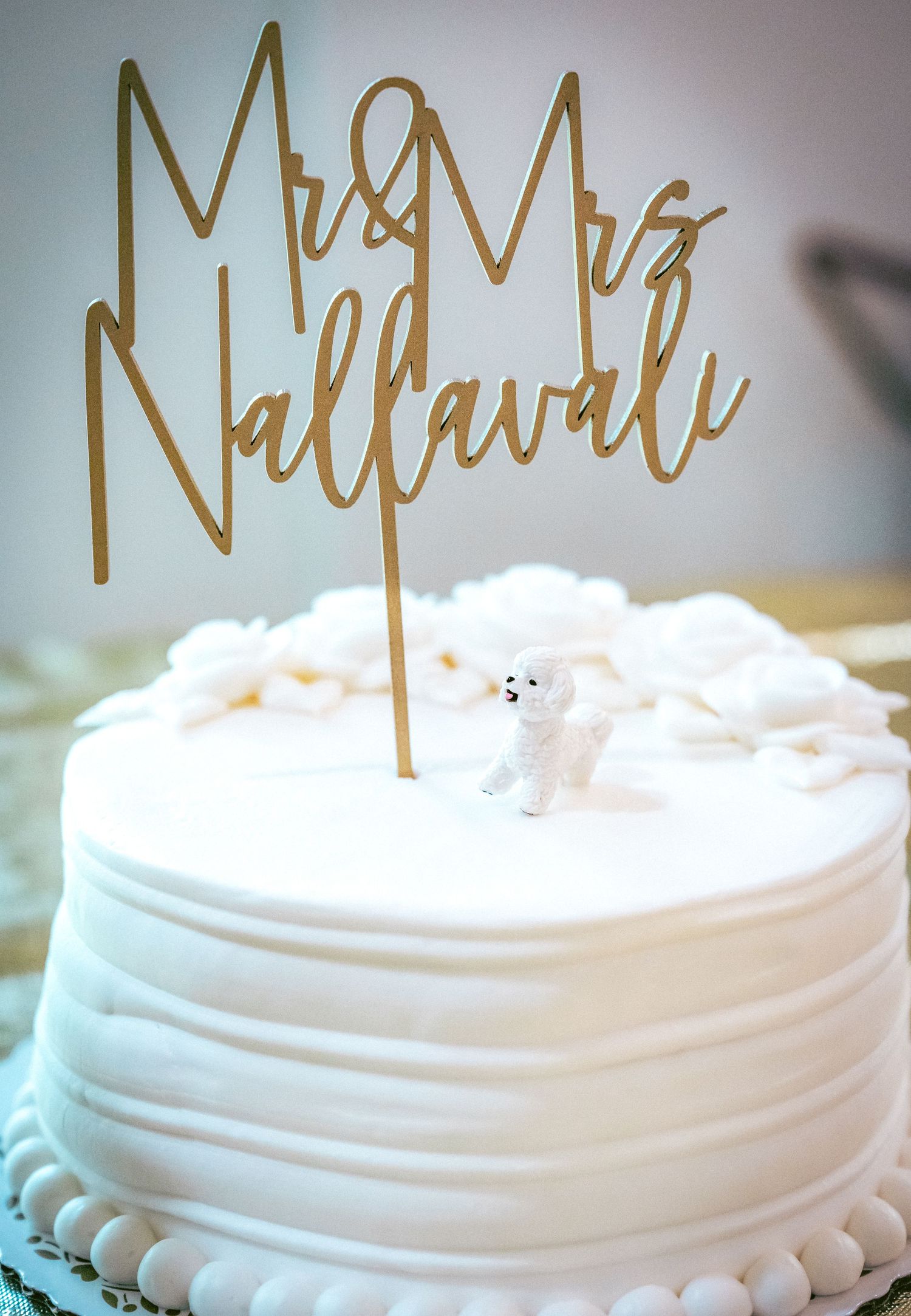 White wedding cake with elegant gold calligraphy topper displayed against a soft blurred background.