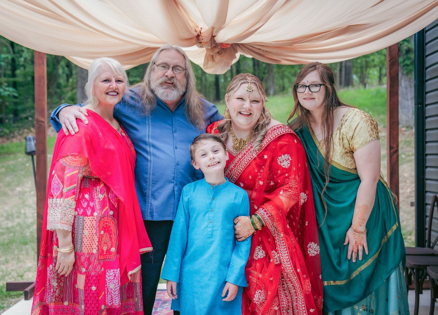 Family and friends pose together at an outdoor Indian wedding celebration under peach drapes.