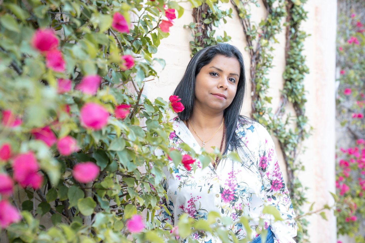 A person stands among vibrant pink flowers and lush greenery in a garden setting.