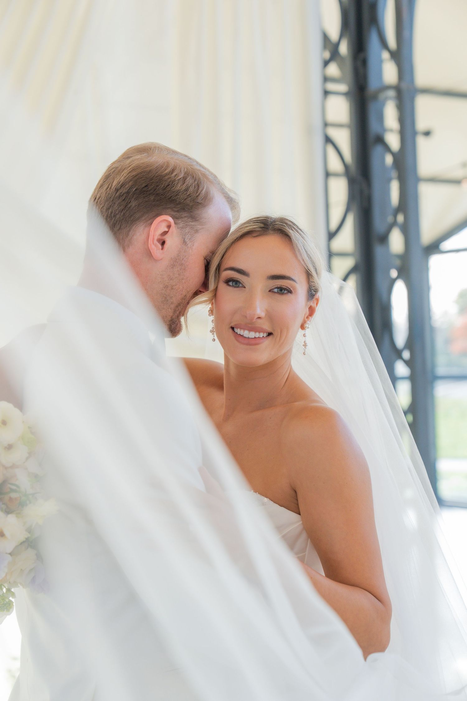 Intimate wedding portrait moment captured against white draping and natural light.