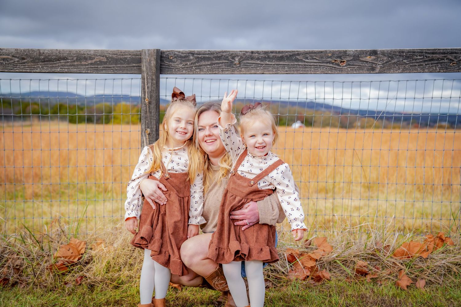 Family photoshoot in rustic field setting with wooden fence and autumn colors.