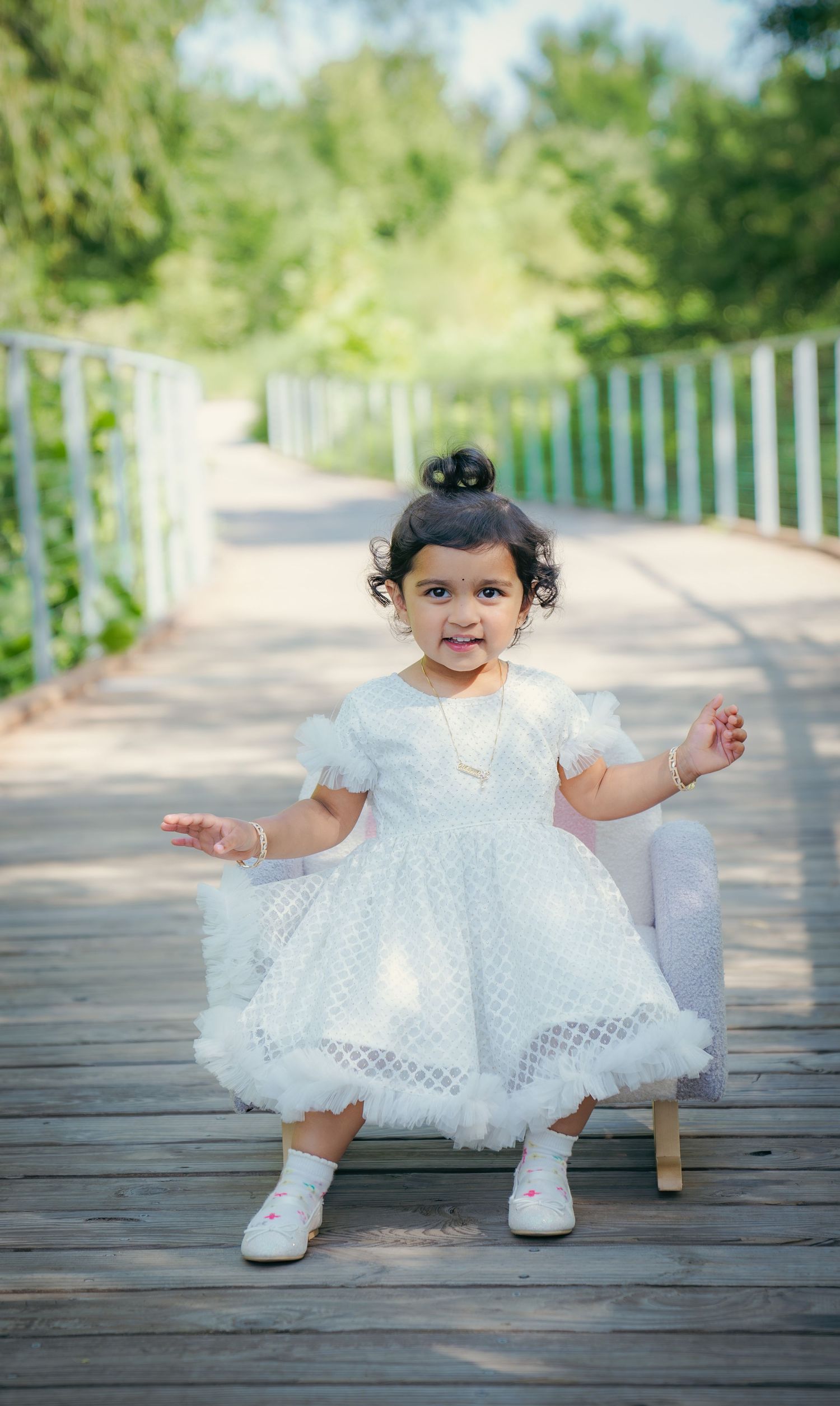 Sweet toddler in white dress playing on wooden boardwalk outdoors.