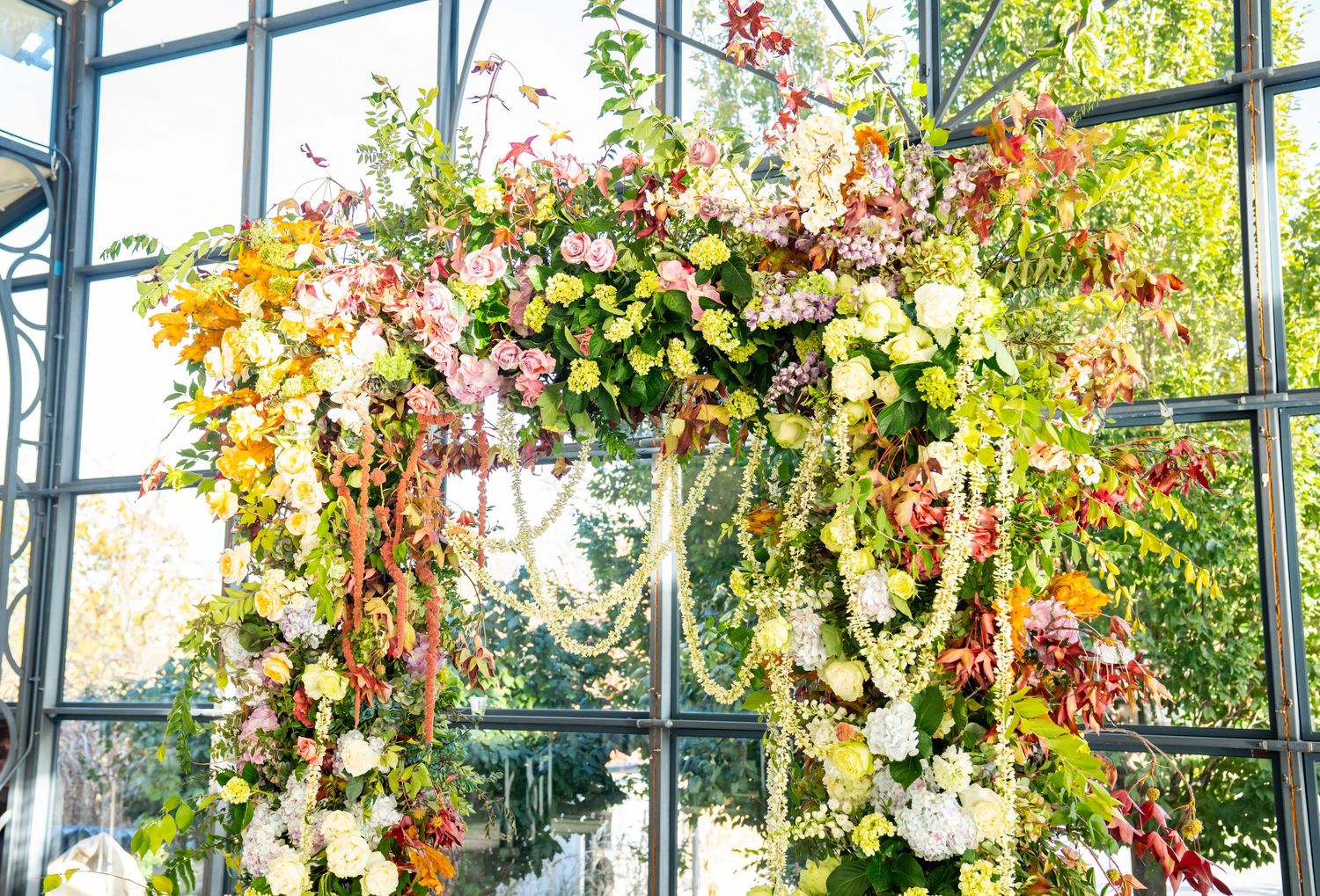 Stunning floral arch with pink and yellow blooms against glass windows in an event space.