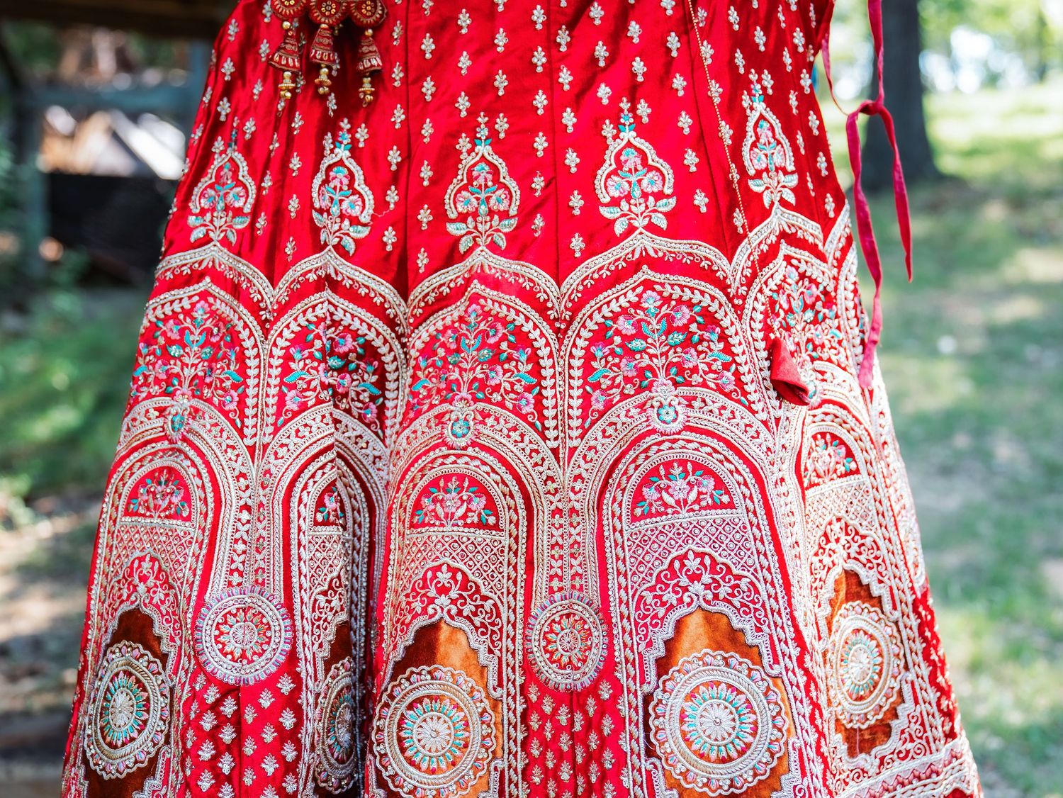 Detailed view of a red bridal lehenga showing ornate silver embroidery and traditional architectural patterns.
