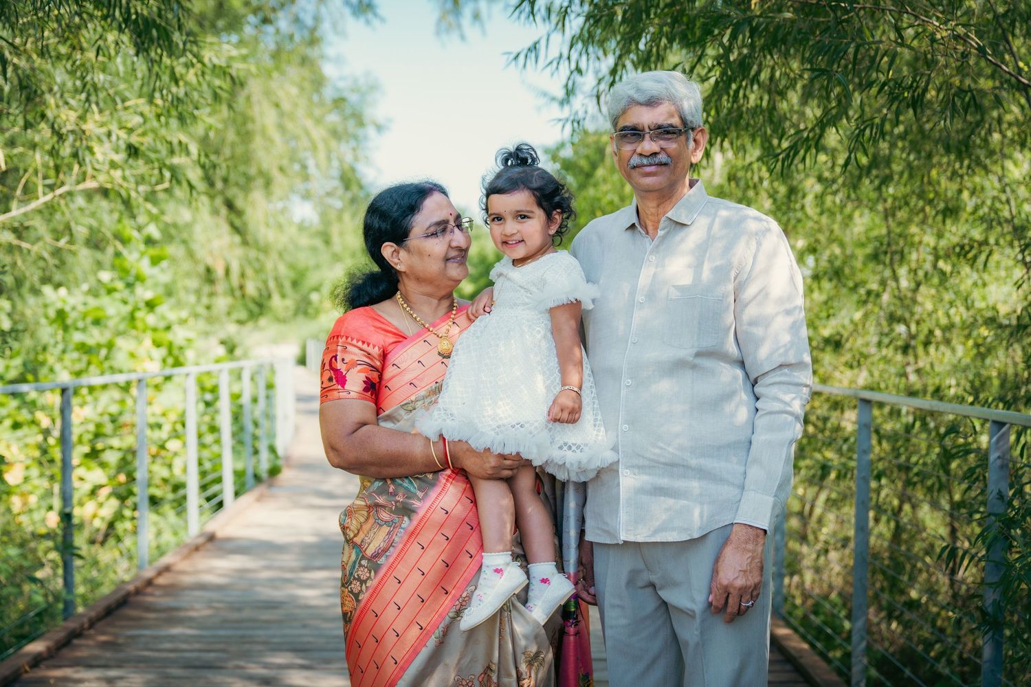 Family portrait in casual attire against lush green outdoor backdrop.