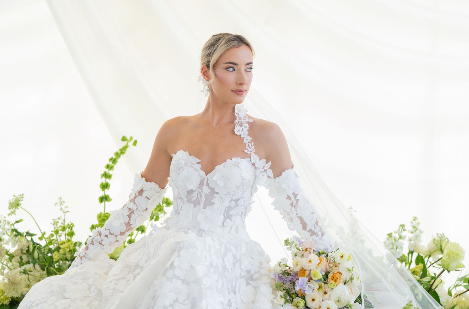 Classic white bridal gown with floral details and flowing veil in garden setting.