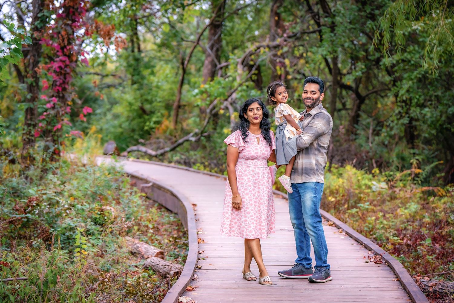 A couple walking on a curved wooden boardwalk surrounded by autumn foliage and red berries.