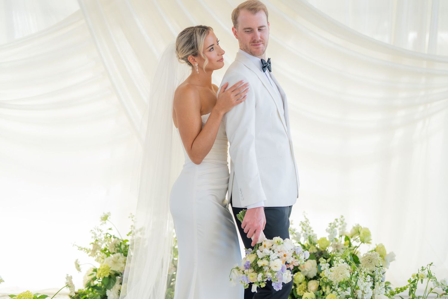 Wedding couple shares intimate moments in a beautifully decorated white tent setting.