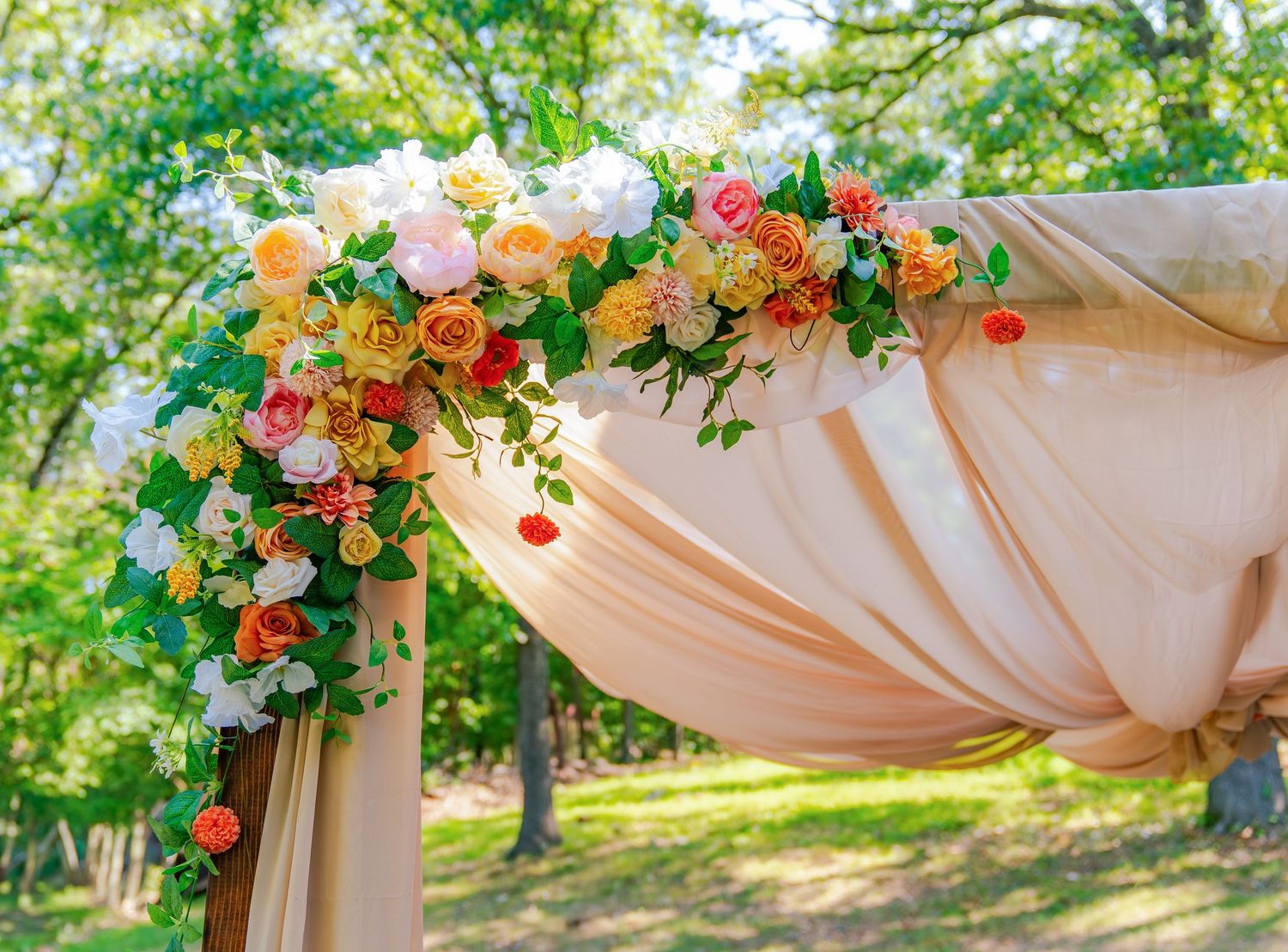 Peach and white fabric draping decorated with floral arrangements for an outdoor wedding.