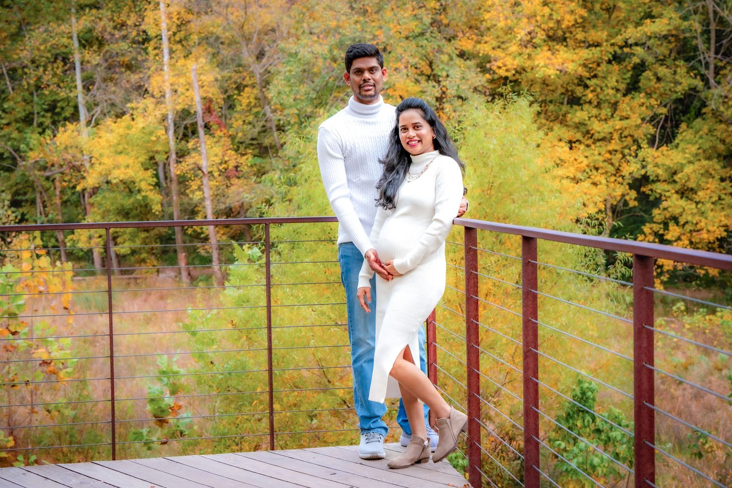 A couple poses on a rustic bridge surrounded by vibrant fall foliage.