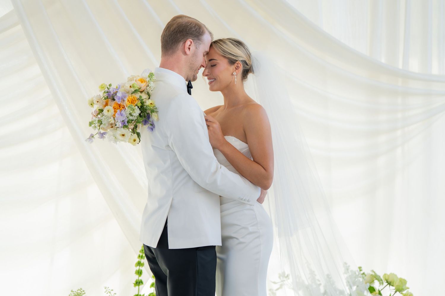 Newlyweds embrace in a light-filled tent with delicate floral arrangements.