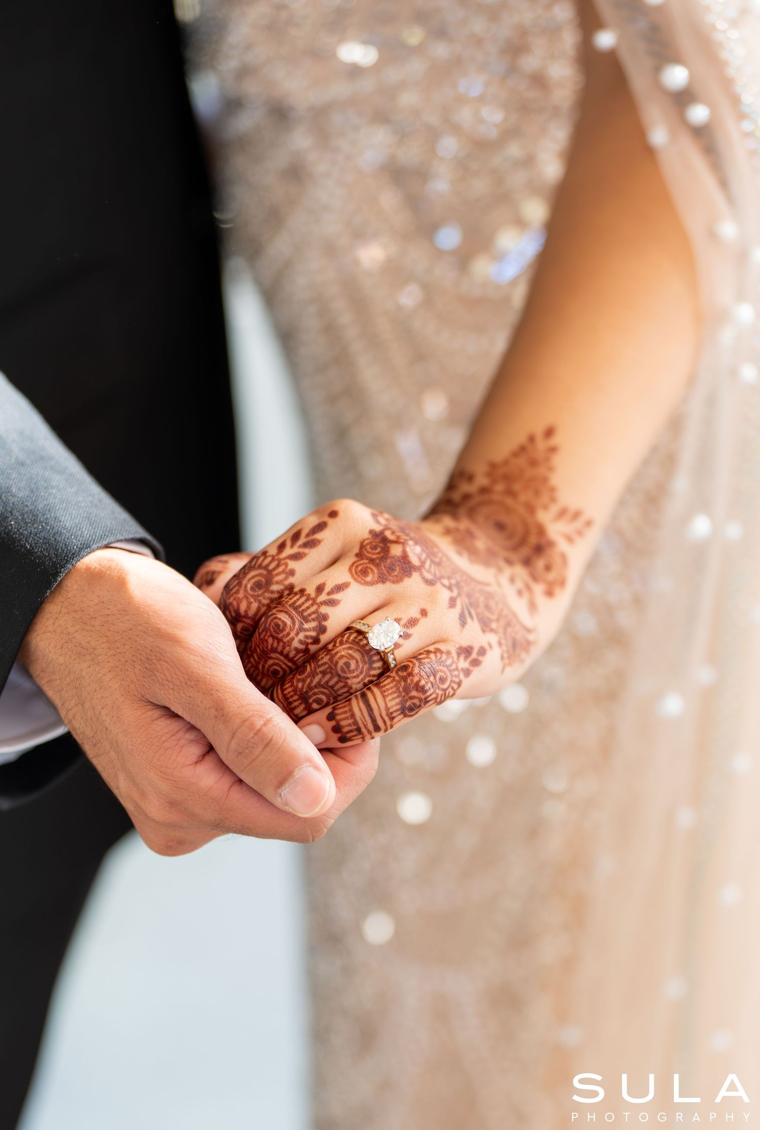 Close-up of intricate henna designs on hands with sparkly fabric in the background.