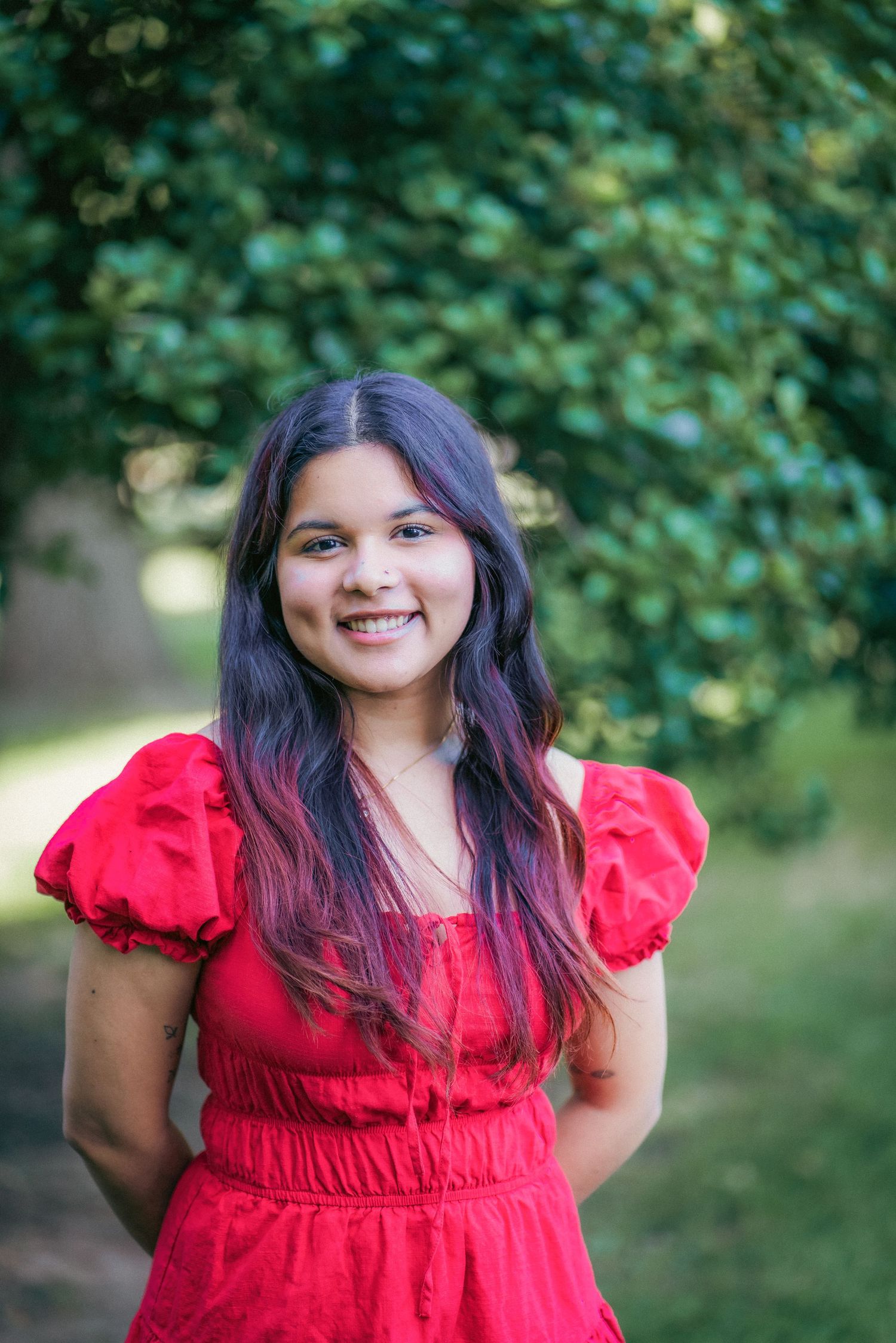 Portrait in a red dress with puff sleeves against a natural green background.