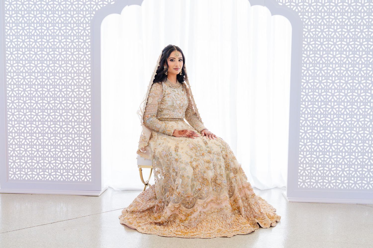 Full-length shot of bride in cream and gold wedding attire against white backdrop.