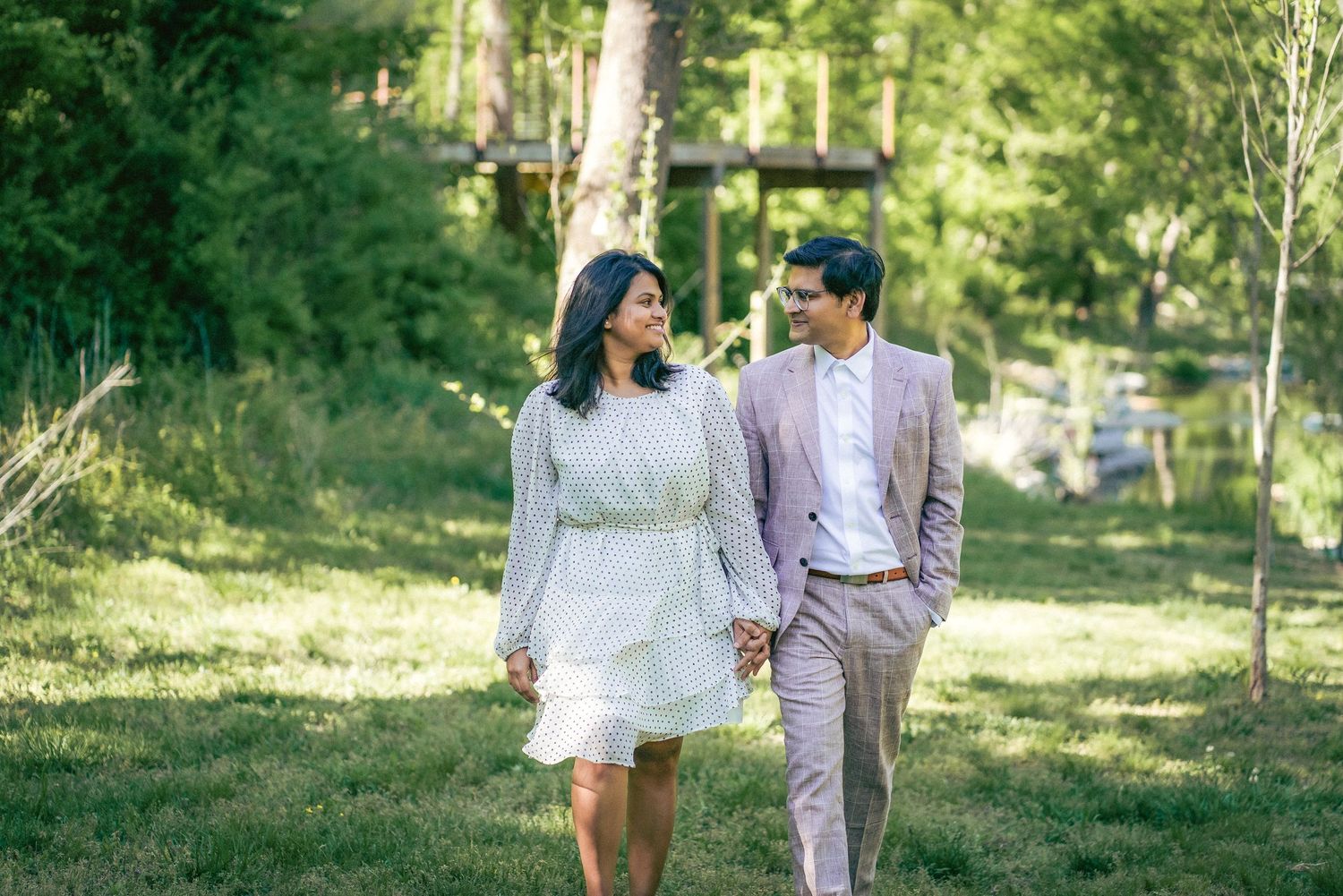 A couple walks together through a sunlit wooded path during a romantic outdoor photoshoot.