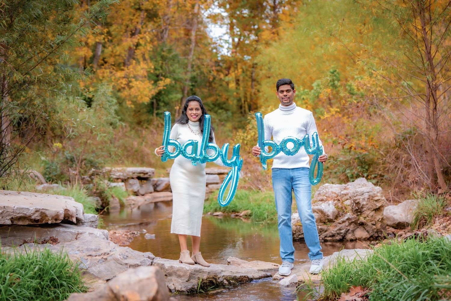 A couple poses together by a stream with autumn foliage creating a warm natural backdrop.