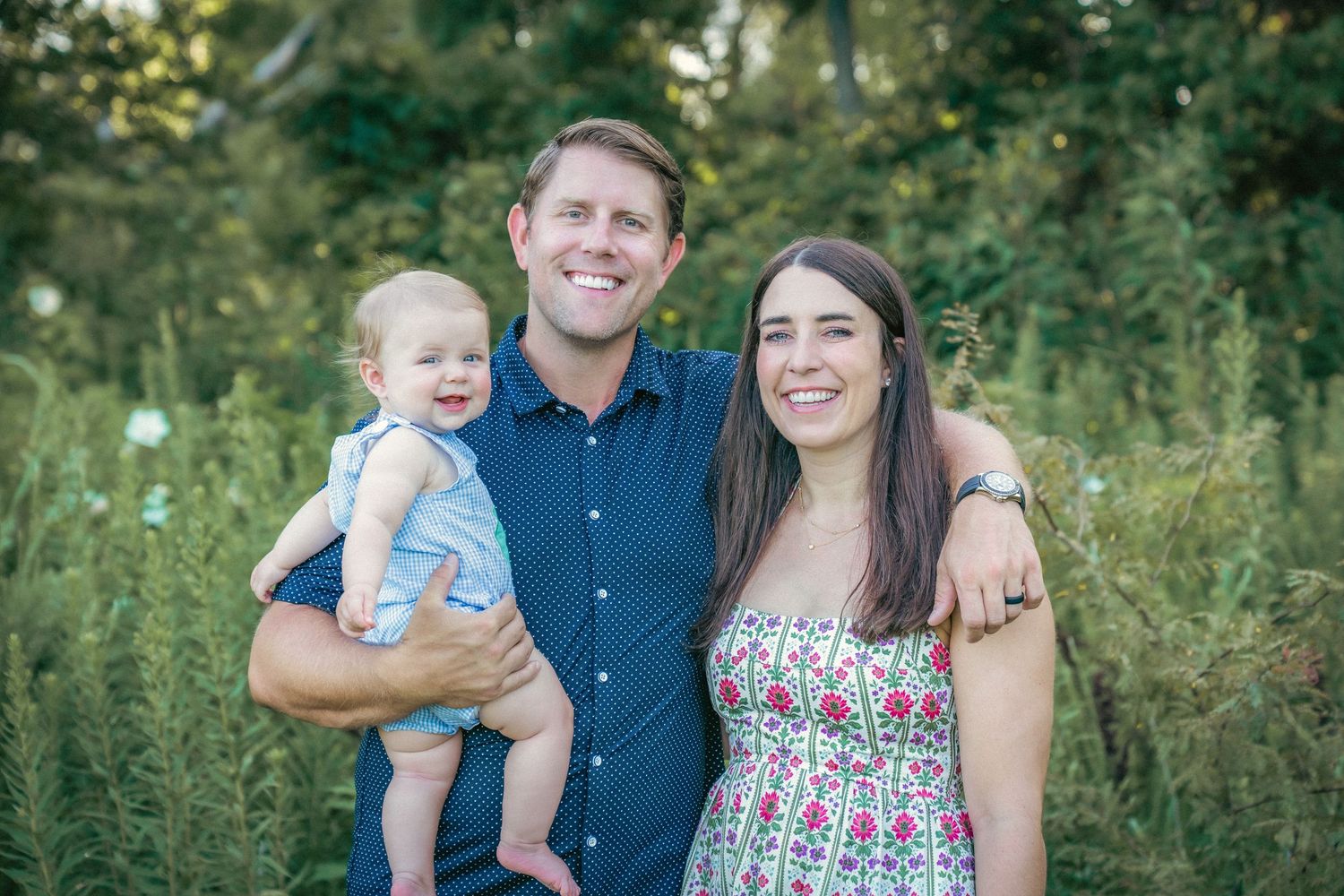Family poses together outdoors in coordinated outfits against a natural green background.