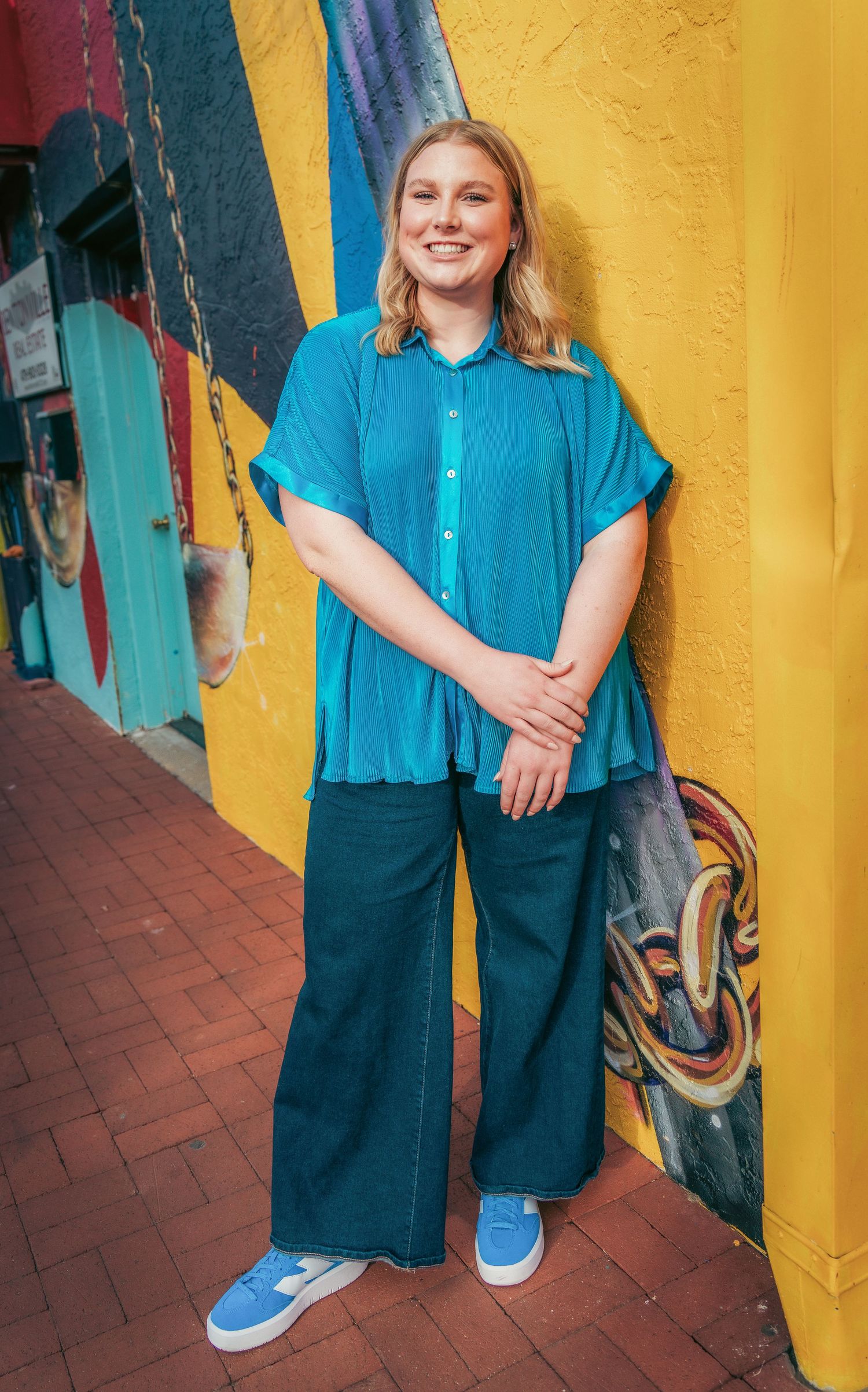 Casual turquoise top paired with dark pants and blue sneakers against colorful walls.