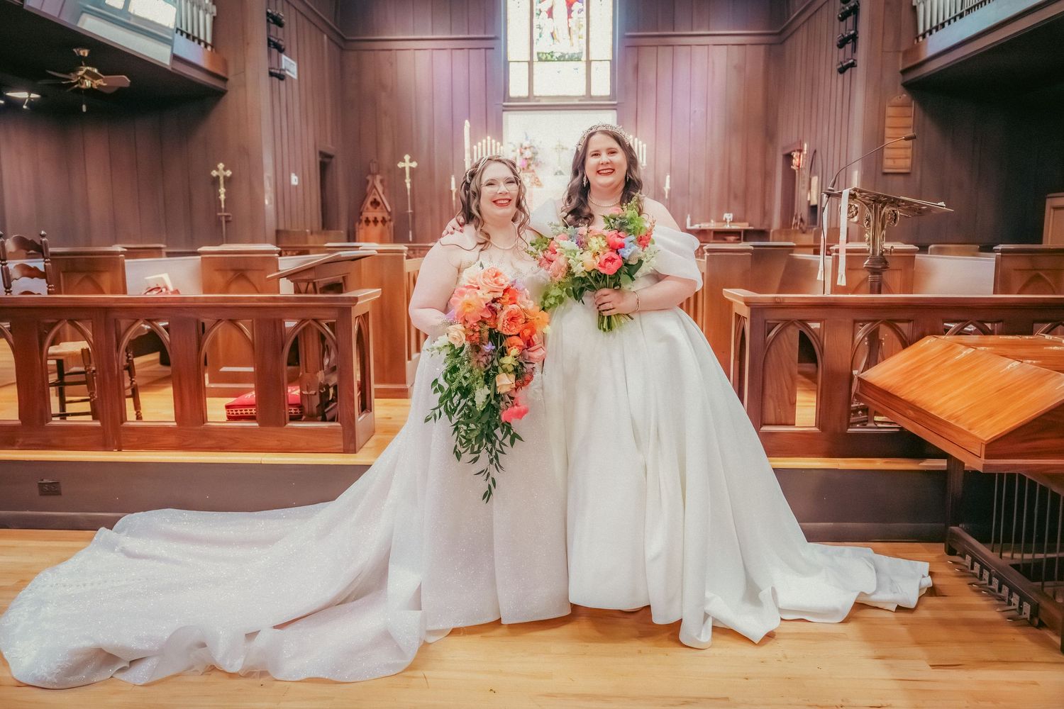 Two brides in matching white gowns share a special moment in a church sanctuary.