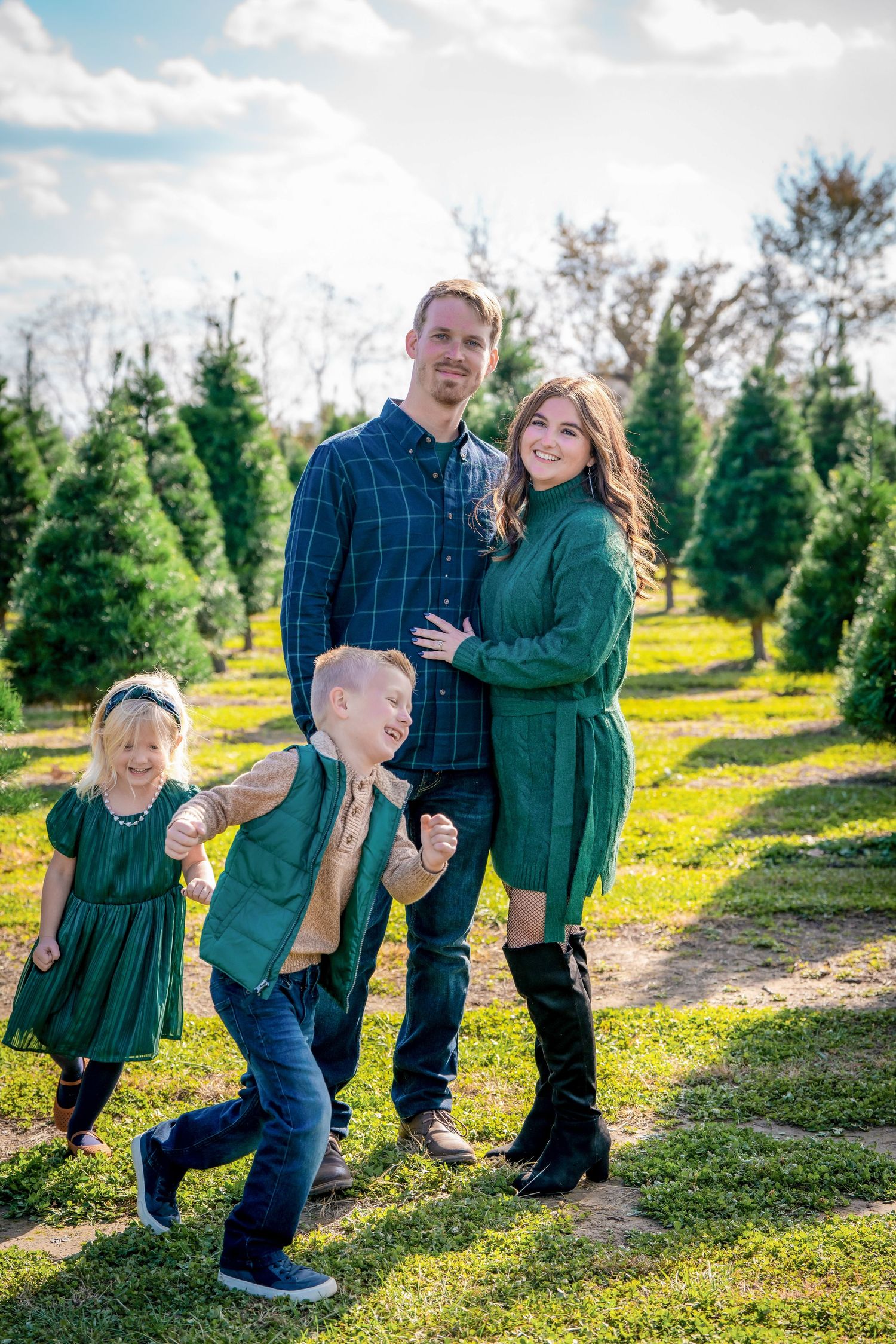 Family wearing coordinating green outfits playing together at a Christmas tree farm.