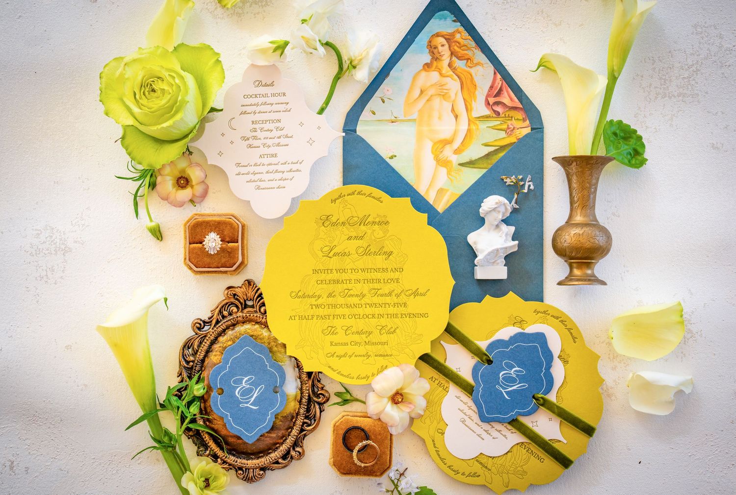 Decorative wedding invitation suite with yellow flowers and blue accents laid out on white surface.