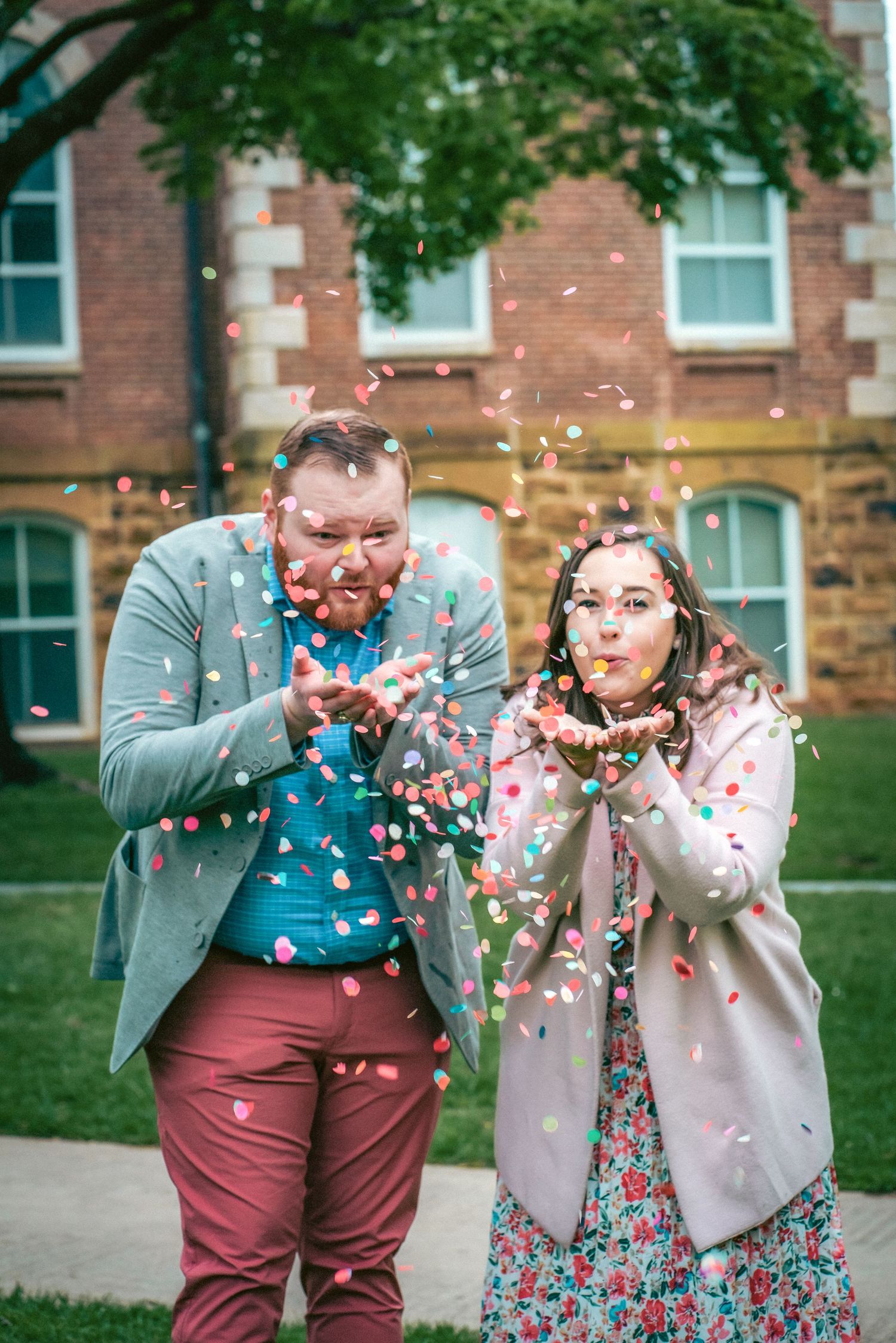 Couple blowing confetti in front of historic brick building during outdoor photo session.