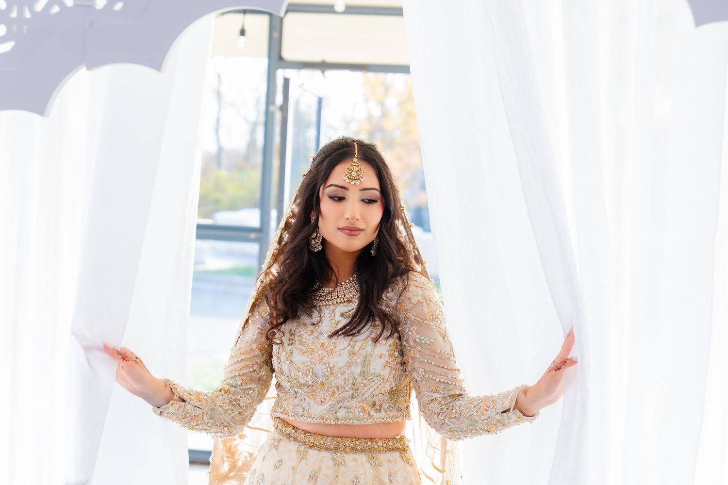 Elegant bride in ivory embroidered lehenga poses against white backdrop.