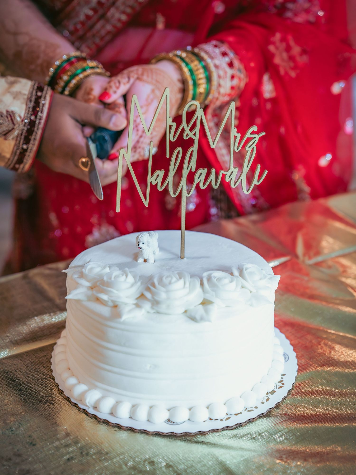 White wedding cake with decorative topper displayed on gold tablecloth.
