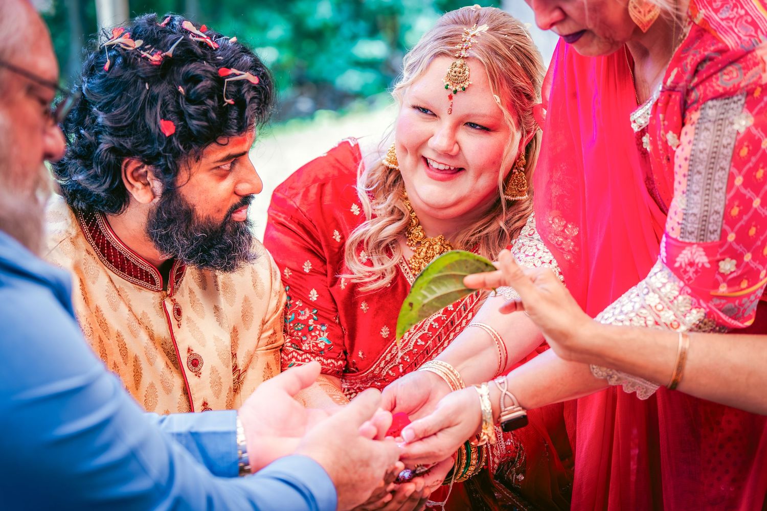 Traditional Indian wedding ceremony showing hands exchanging rings against vibrant red attire.