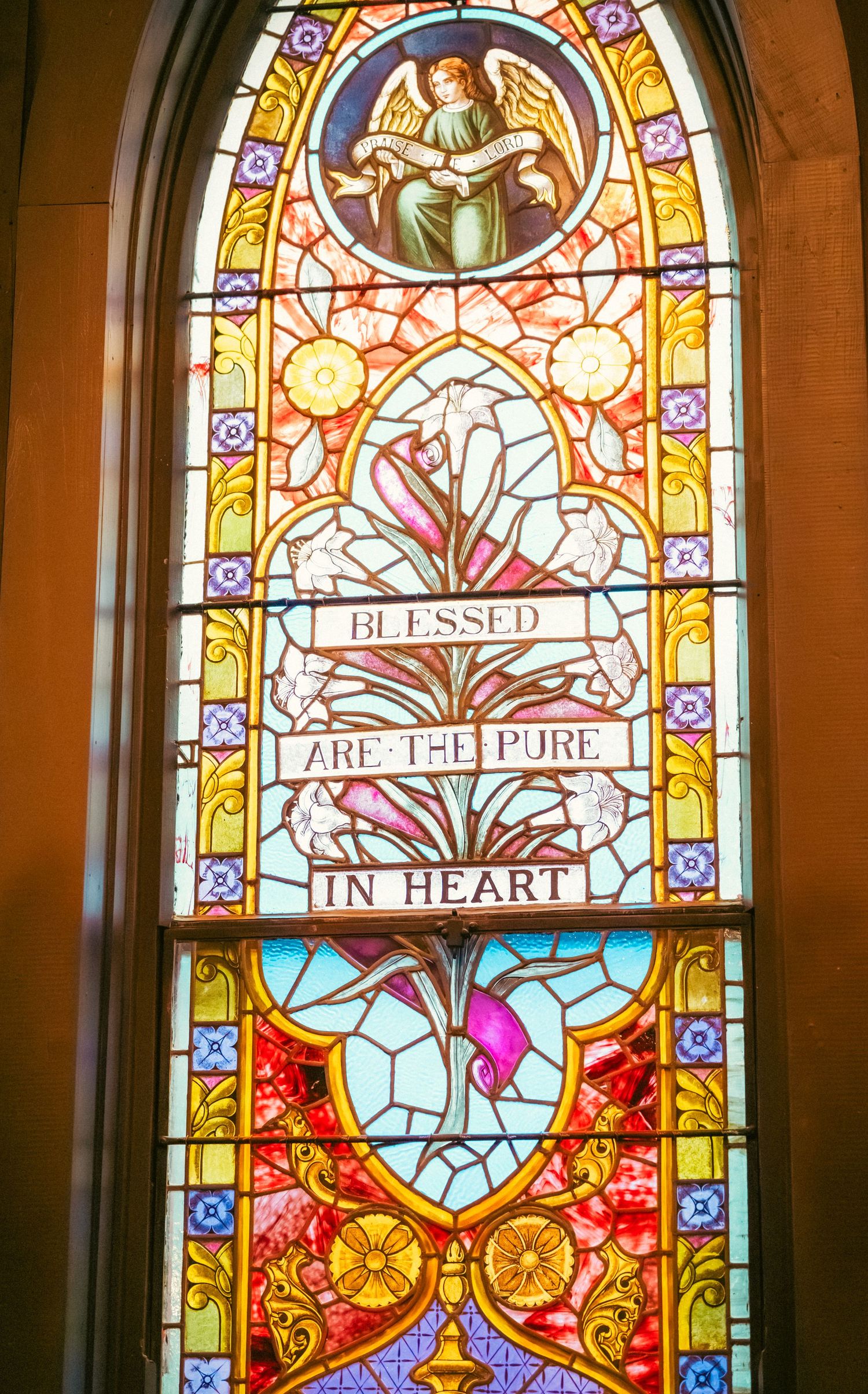 Ornate stained glass church windows with religious text and floral designs in vibrant colors.