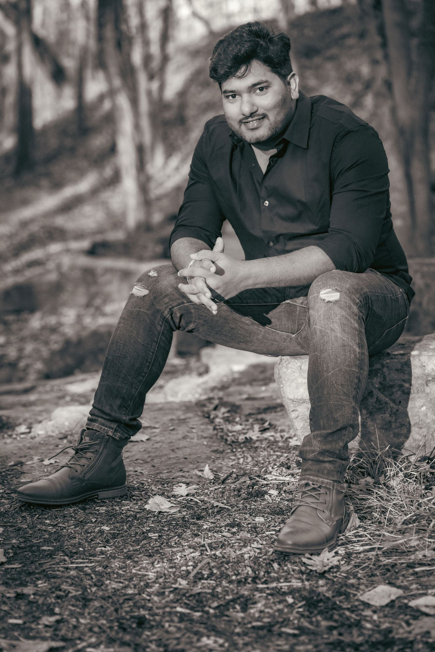 A casual portrait session in black and white showing a person resting on fallen leaves in the woods.