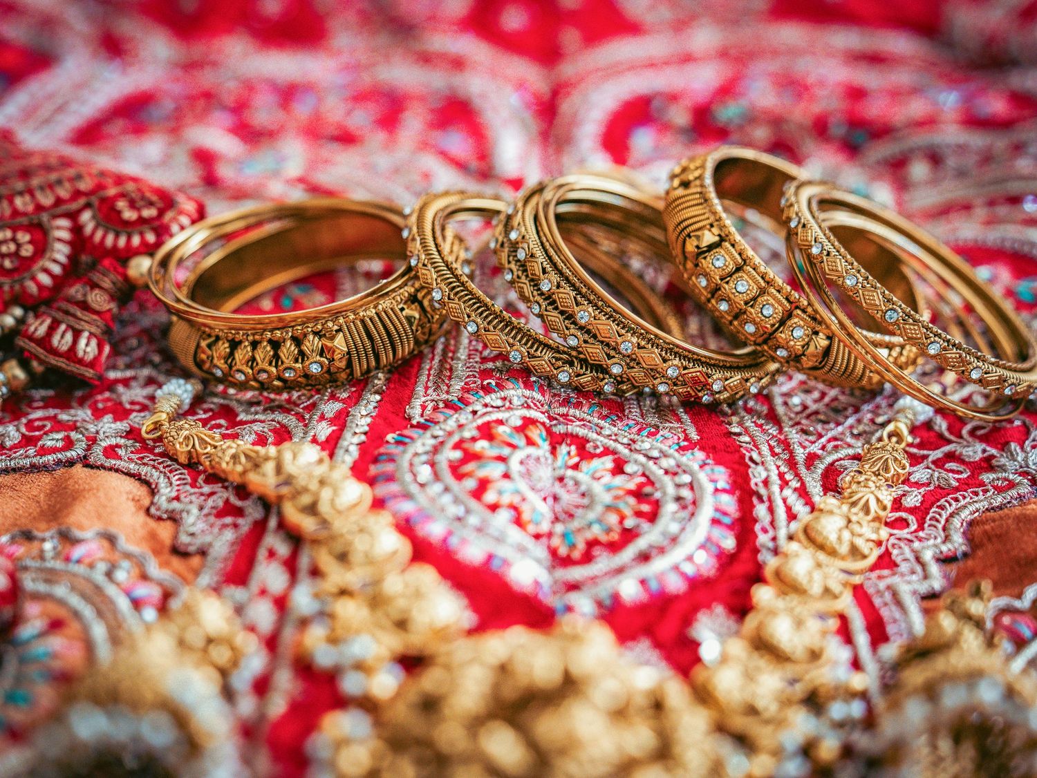 Gold wedding bangles and traditional jewelry arranged on a red embroidered fabric with intricate patterns.