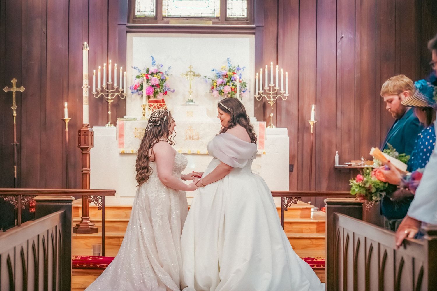 A tender moment between two people in white wedding gowns inside a traditional church.