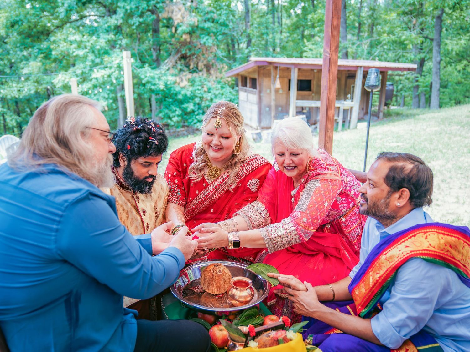 Couple participates in a traditional Indian wedding ceremony ritual under an outdoor tent canopy.