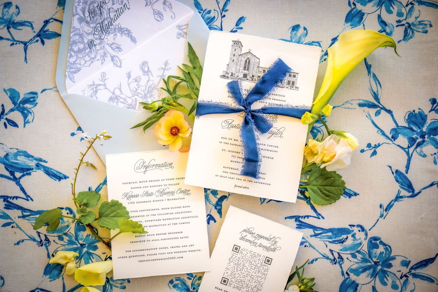 Wedding invitations with blue ribbon and floral pattern displayed on patterned fabric.