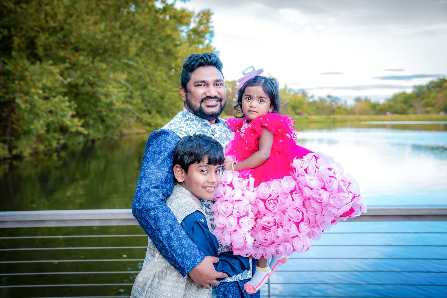 Family in coordinated pink and blue outfits poses by a lake during sunset.