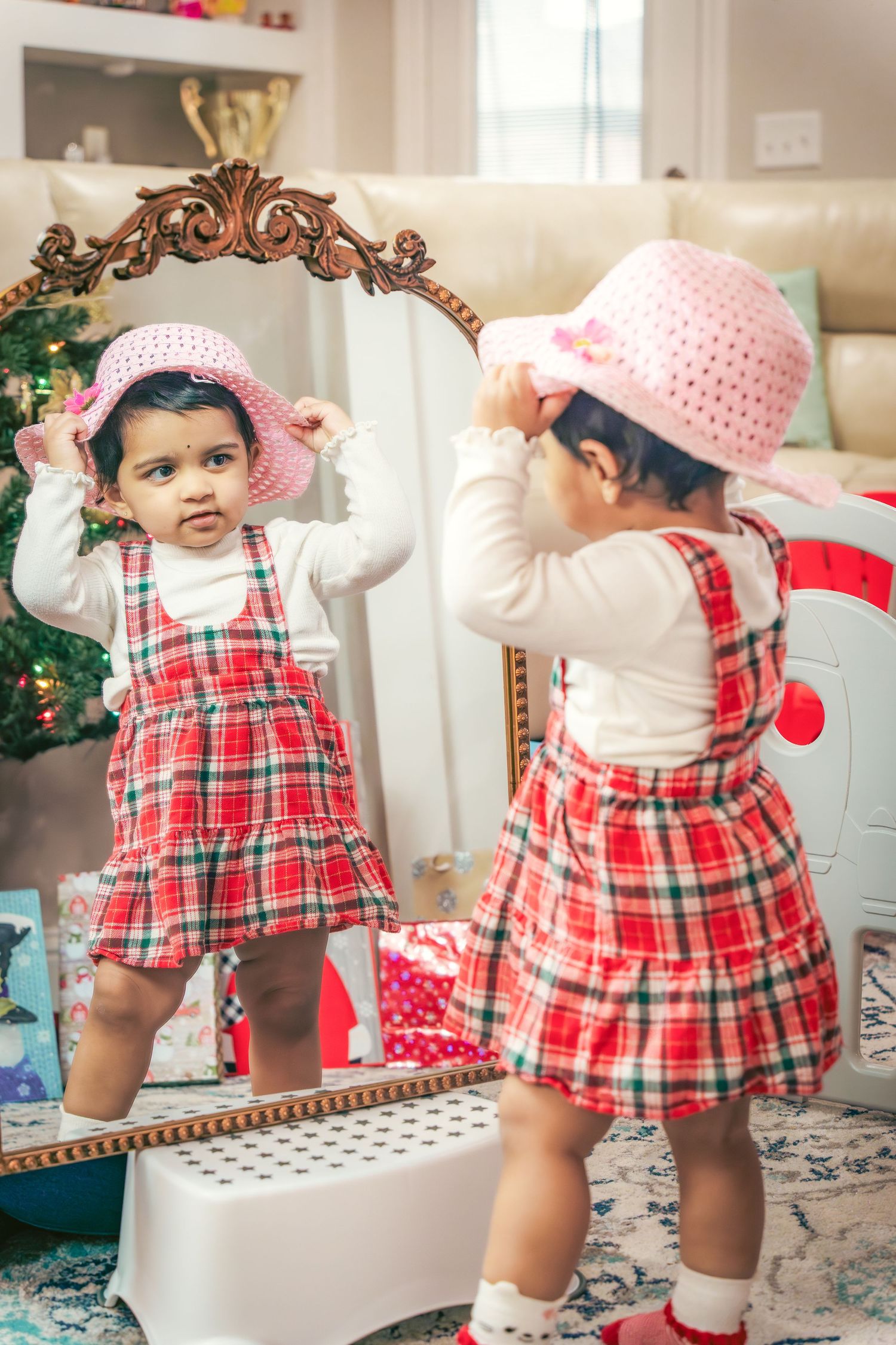 A child in a red plaid dress plays near a decorative mirror during the holiday season.
