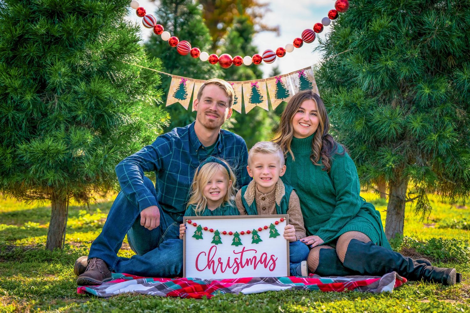 Family photo session with Christmas decorations and red garland at a tree farm.
