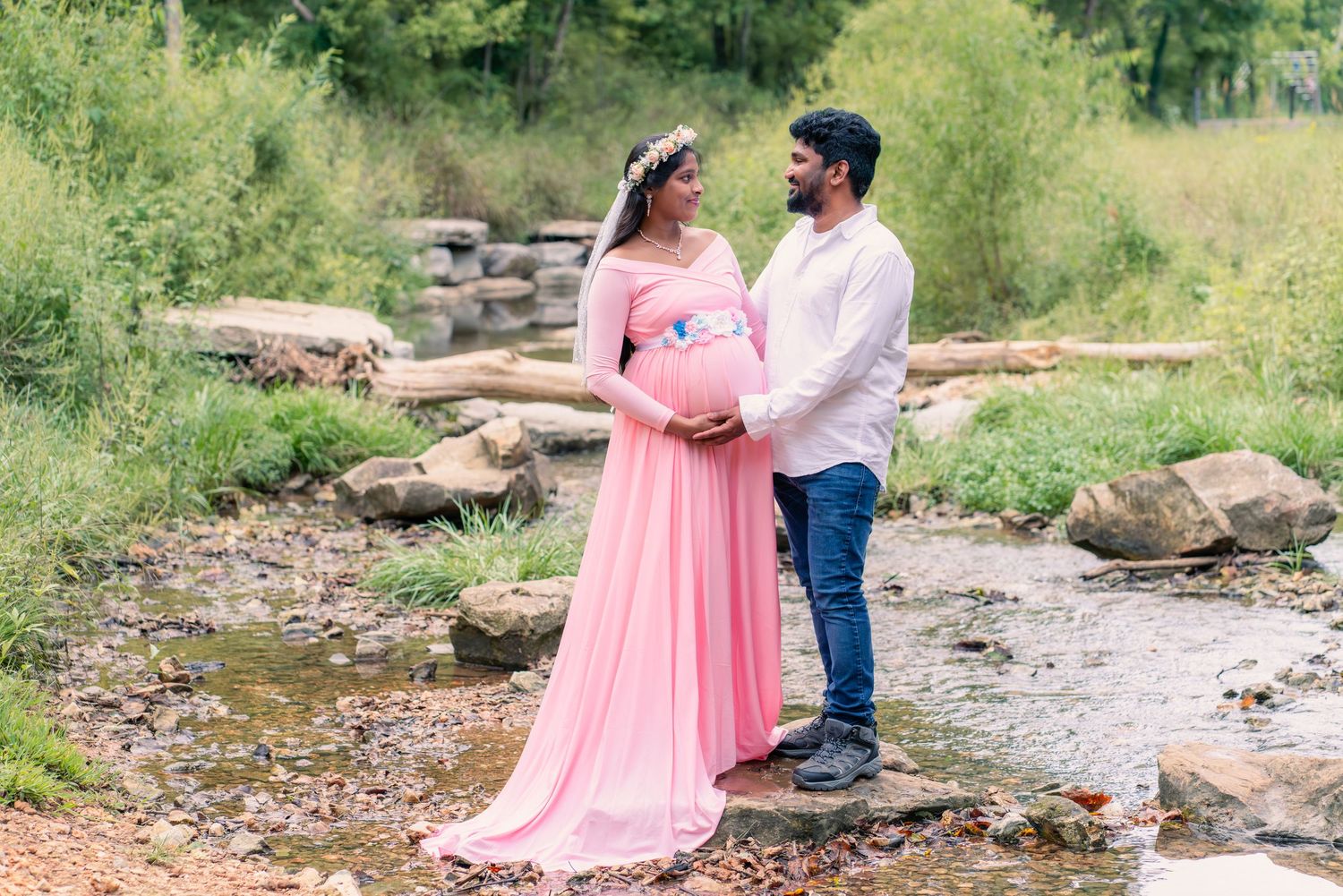 Couple in pink dress and casual wear posing together in outdoor natural setting with rocks and greenery.