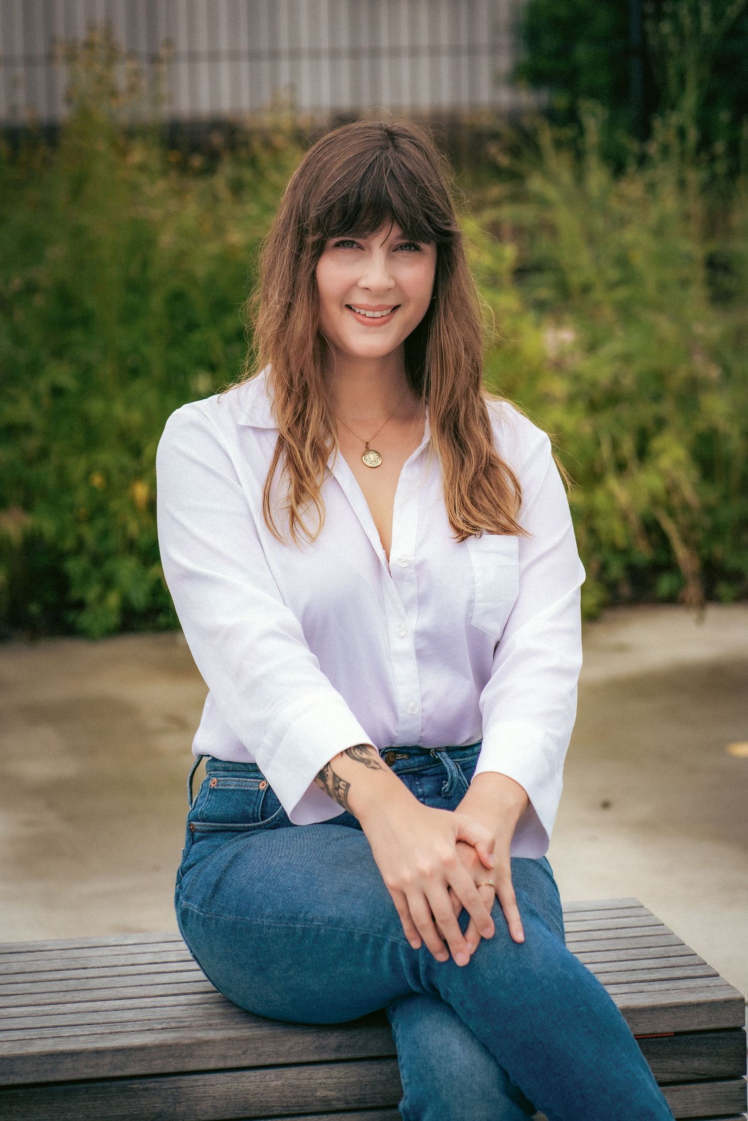A person in a white shirt and jeans sits on a wooden bench outdoors.
