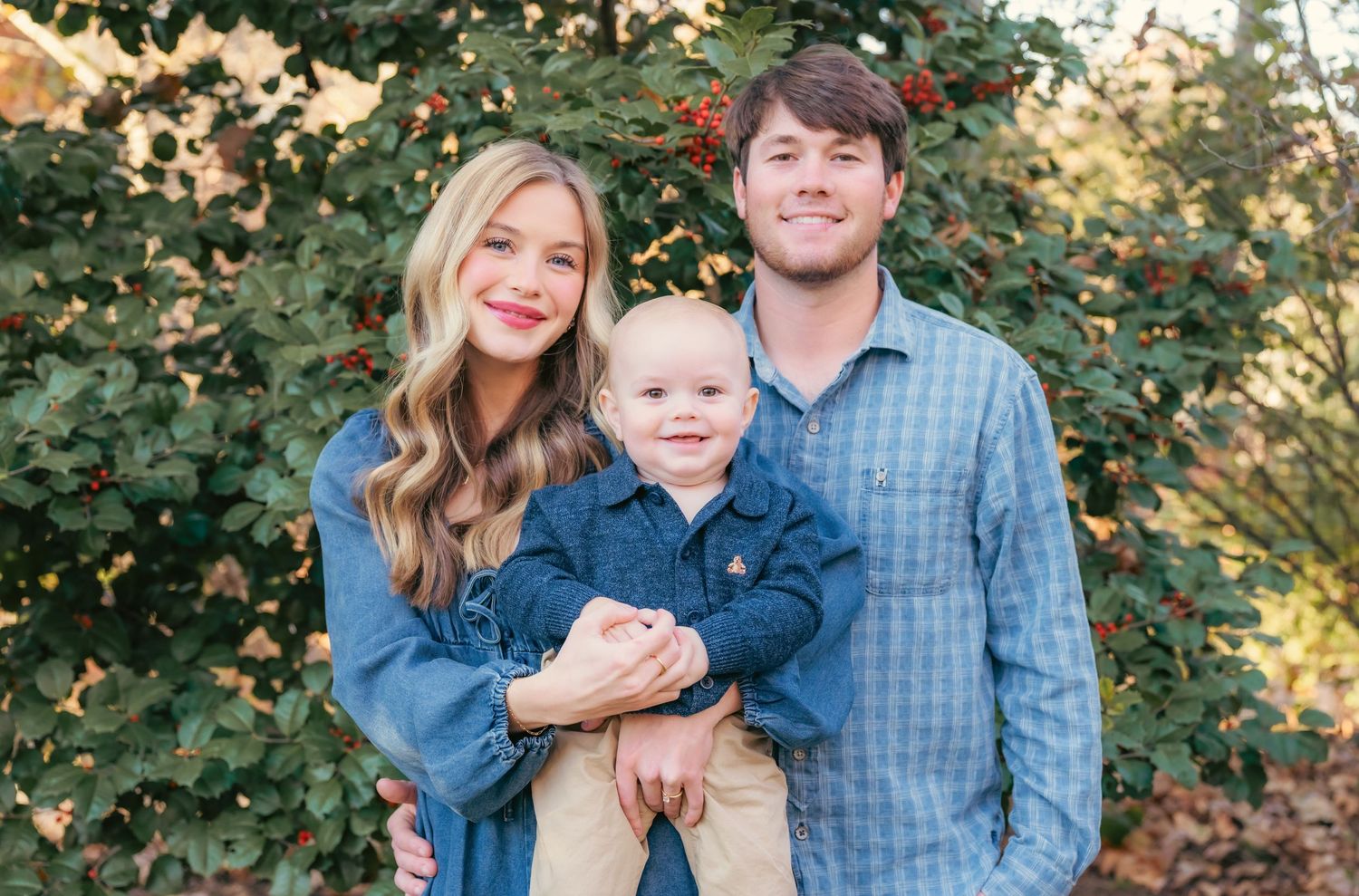 Family in casual blue and plaid outfits posing outdoors with trees in background.
