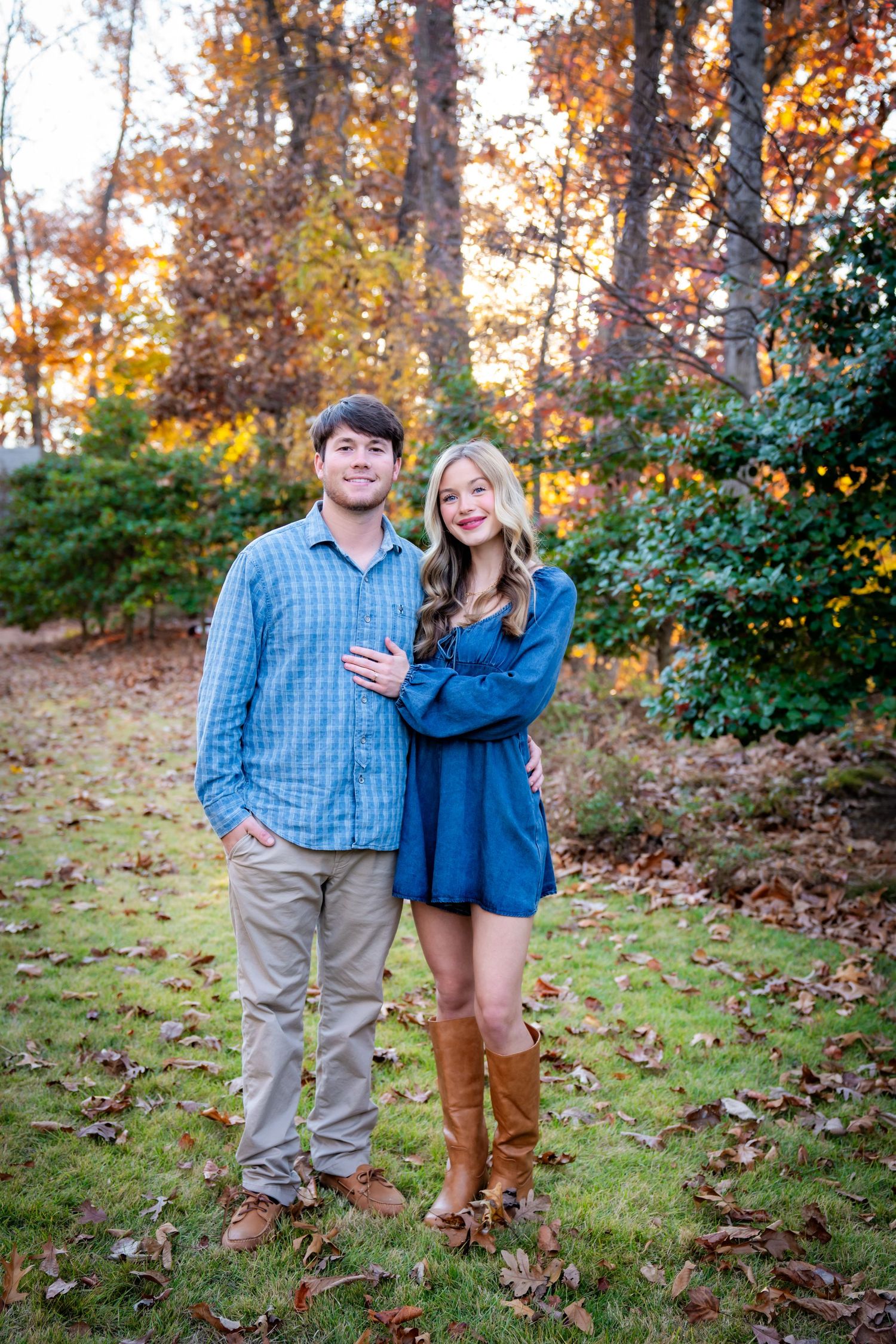 Couple in coordinated casual outfits posing on grassy hill during fall season.