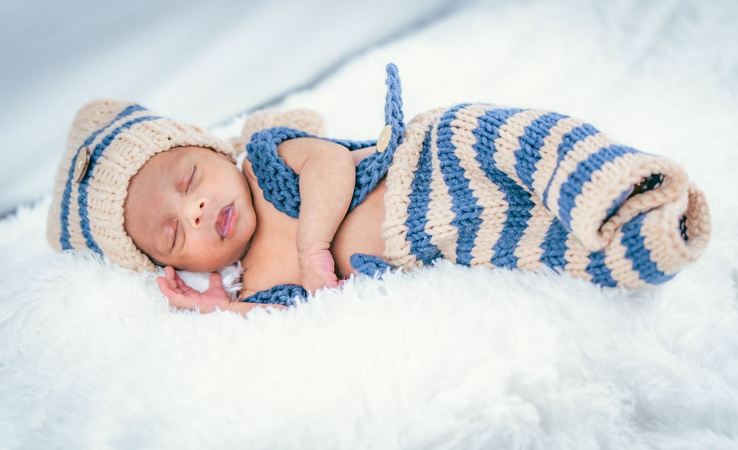 Sleeping newborn wrapped in blue and white striped accessories on soft white bedding.